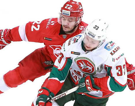 На изображении два хоккеиста в борьбе за шайбу на льду. Один в красной форме с номером 22, другой в белой форме с зелеными и красными элементами и номером 33. Оба активно играют, концентрируясь на контроле шайбы