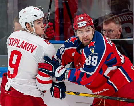 На изображении двое хоккеистов на льду. Игрок в белой форме с номером 9 противостоит игроку в синей форме с номером 89. Они ведут силовую борьбу у борта. Вдали видны зрители